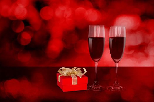 Two wineglasses and red gift box on desk with red blur bokeh background, champagne glasses and presents with celebration and anniversary, love and romantic, valentine day concept.
