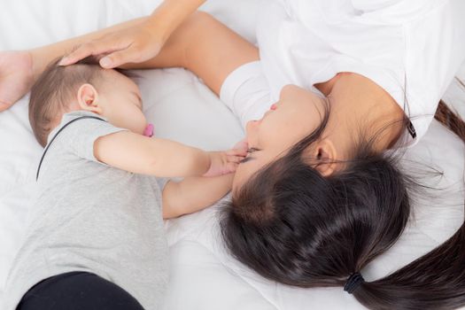 Young asian mother touch head of little baby girl with tender on bed in the bedroom, mom love newborn and care, woman with expression with child together, parent and daughter, family concept.