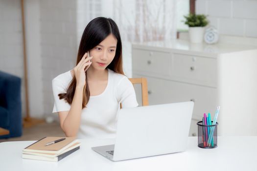 Young asian woman talking phone and work from home with laptop computer, freelance using notebook to internet online and speak on smartphone, domestic life, business and communication concept.