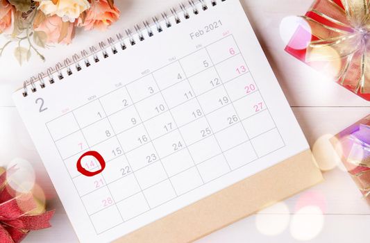 Calendar and flower with memo 14 February Valentine day on desk with blur bokeh background, reminder for surprise of love, romance and sweet, celebration and decoration, top view, holiday concept.
