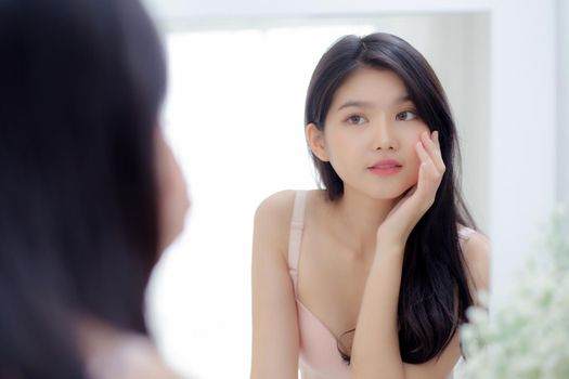Beautiful young asian woman smiling look at mirror of checking face with skin care and cosmetic for rejuvenation and hygiene, beauty girl happy clean facial with cream or lotion and for health.