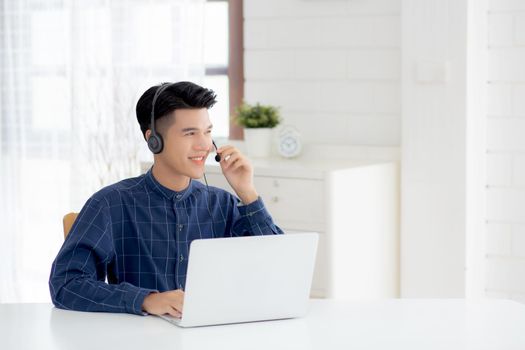 Young asian businessman working on laptop computer wearing headphone at home, business man wearing headset for video conference, communication and education, male study and learning for e-learning.