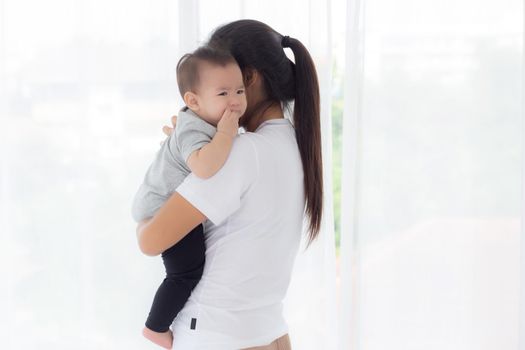 Young asian mother holding little baby girl and walking together in the bedroom at home, mom carry daughter and care, relationship of parent and child, toddler and parent, indoor, family concept.