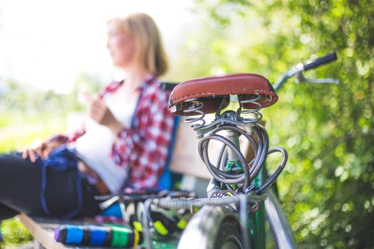 Closeup picture of brown vintage bicycle seat, blonde girl sitting in blurry background