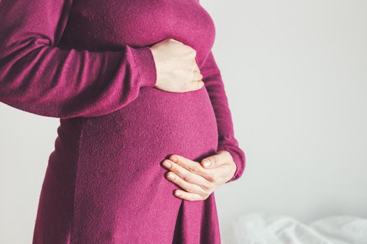 Close up of pregnant tummy, Caucasian mother in magenta dress