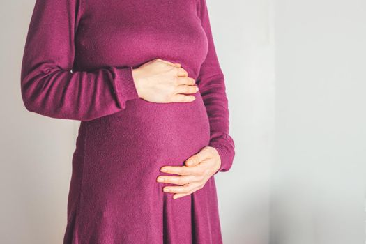 Close up of pregnant tummy, Caucasian mother in magenta dress
