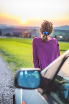 Young woman sitting on a car, enjoying the sunset