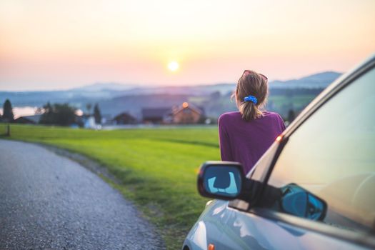Young woman sitting on a car, enjoying the sunset