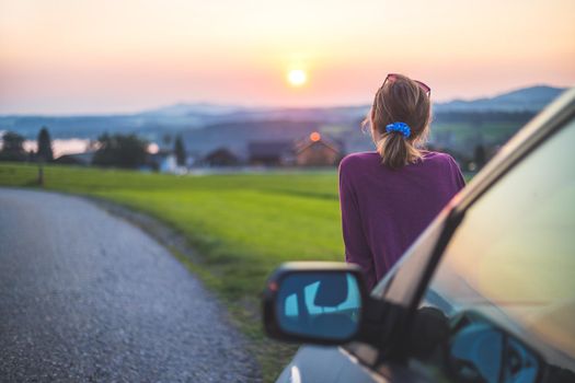 Young woman sitting on a car, enjoying the sunset