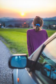 Young woman sitting on a car, enjoying the sunset
