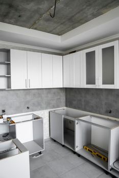 Custom kitchen cabinets installation with a furniture facades mdf. Gray modular kitchen from chipboard material on a various stages of installation. A frame furniture fronts mdf profile