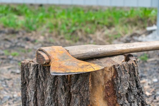 An old and rusty work ax lies on a rotten stump