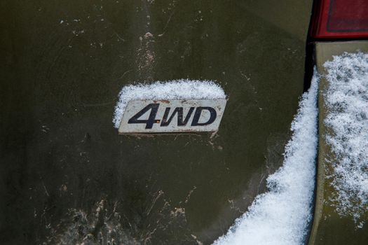 an abbreviation 4wd - four wheel drive - on dirty green car back, with snow
