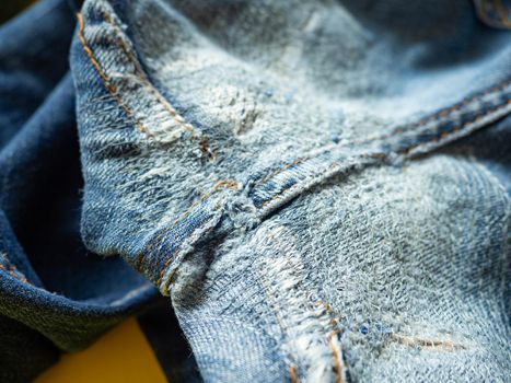 Blue jeans that have been repaired on the gusset. Placed on a yellow background.