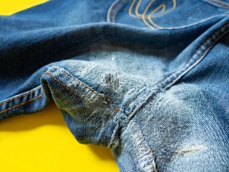 Blue jeans that have been repaired on the gusset. Placed on a yellow background.