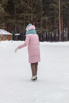 One girl in warm clothes rides on an ice rink near the forest. Winter sports recreation. Entertainment in quarantine