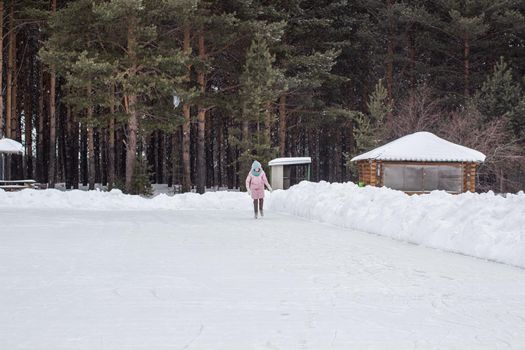 One girl in warm clothes rides on an ice rink near the forest. Winter sports recreation. Entertainment in quarantine