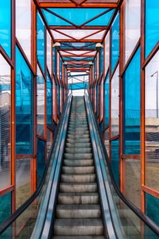 Long escalator to bridge over street with colorful windows around