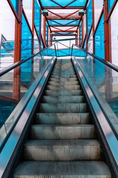 Long escalator to bridge over street with colorful windows around