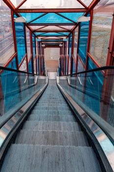 Long escalator to bridge over street with colorful windows around