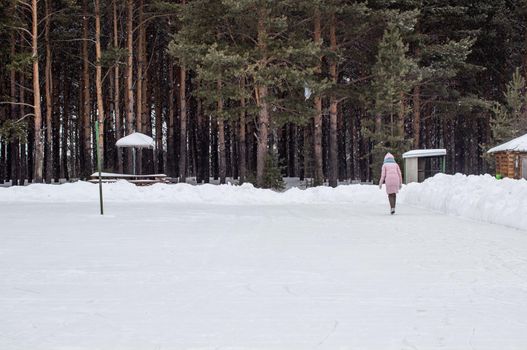 One girl in warm clothes rides on an ice rink near the forest. Winter sports recreation. Entertainment in quarantine