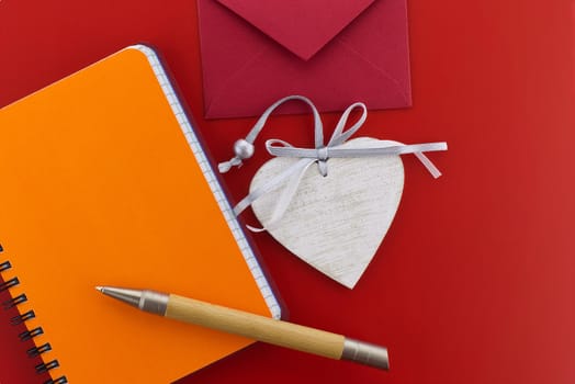 Heart medallion, wire bound notepad, pen and envelope on red background. Greetings and love letter