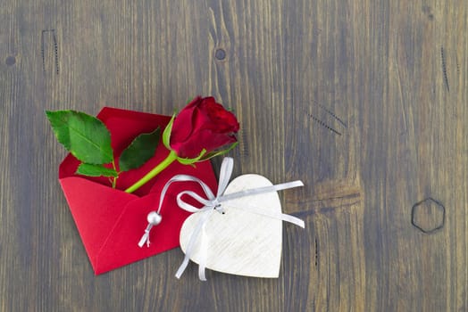 Red rose in envelope and heart medallion on wooden background with free copy space. Wishes, greetings and love message