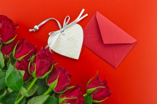 Red roses, envelope and wooden heart medallion on red background with free copy space. Wishes, greetings and love message