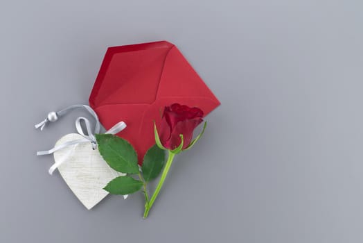 Red rose and wooden heart medallion above the envelope on gray background with free copy space. Wishes, greetings and love message