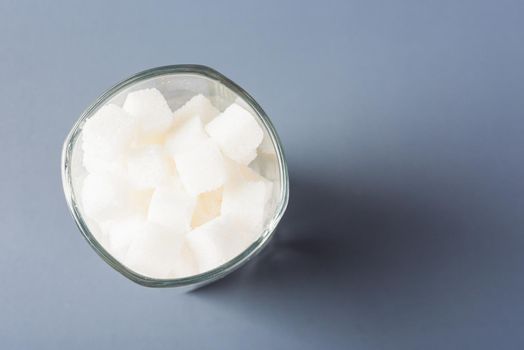 Top view glass full of white sugar cube sweet food ingredient, studio shot isolated on gray background, health high blood risk of diabetes and calorie intake concept and unhealthy drink