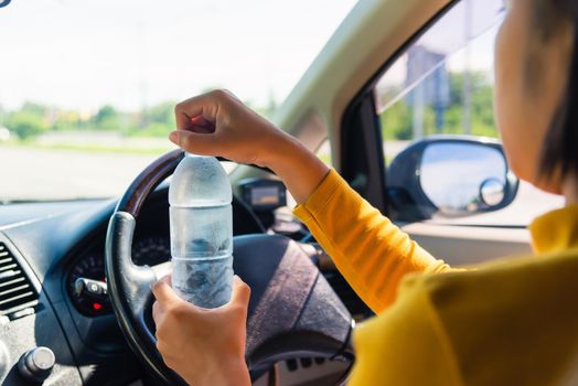 Asian woman holding a water bottle for drink while driving the car in the morning during going to work on highway road, Transportation and vehicle concept