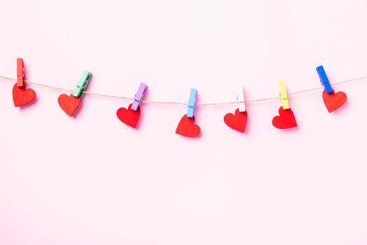 Happy Valentine's day concept. red heart-shaped valentines decoration hanging with wood clips for love on the rope isolated on pink background with copy space