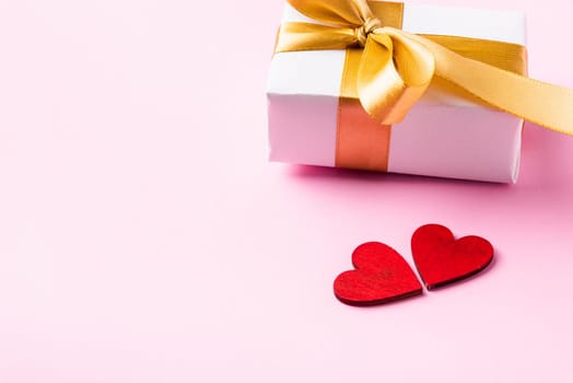 Valentines' day background concept. White gift box with a golden bow ribbon and wood red hearts composition greeting card for happy love isolated on pink background with copy space. View from above