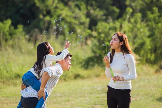 Happy Asian lifestyle family mother, father and little cute girl child having fun together and enjoying outdoor play blowing soap bubbles in the garden park on a sunny day, summertime