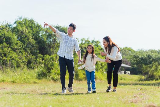 Happy Asian young family father, mother and child little girl having fun and enjoying outdoor walking down the road outside together in green nature park on a sunny summer day