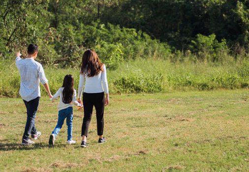 Happy Asian young family father, mother and child little girl having fun and enjoying outdoor walking down the road outside together in green nature park on a sunny summer day