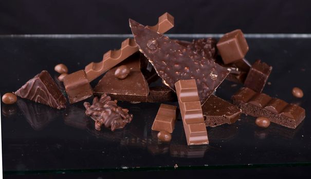 Broken chocolate pieces and cocoa powder on wooden background