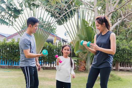 Asian young mother, father and child daughter doing exercising together with dumbbells is fun outdoors in nature a field garden park. Happy family kid sport and exercises for healthy lifestyle