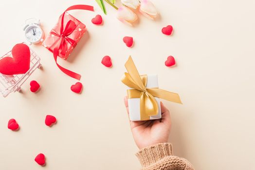 Valentine's day and birthday. Woman hands holding gift or present box decorated and red heart surprise on cream pastel background, Female's hand hold gift box package in craft paper Top view flat lay