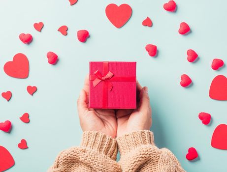 Valentine's day and birthday. Woman hands holding gift or present box decorated and red heart surprise on blue background, Female's hand hold gift box package in craft paper Top view flat lay