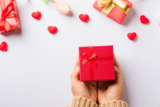 Valentine's day and birthday. Woman hands holding gift or present box decorated and red heart surprise on white background, Female's hand hold gift box package in craft paper Top view flat lay