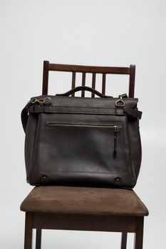 Brown men's shoulder leather bag for a documents and laptop on a brown chair with a white background. Mens leather brief case, messenger bags, leather satchel, handmade briefcase