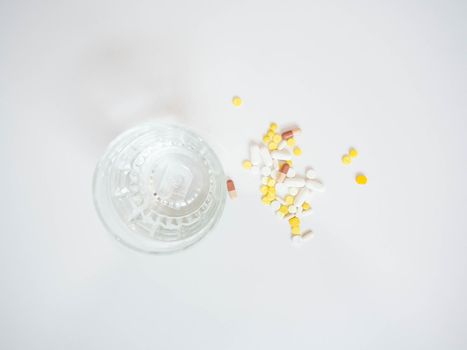 Multi colored pills with a glass of water placed on a white background