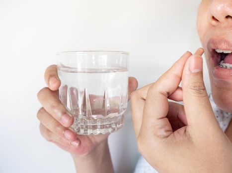 A woman taking a pill into her mouth The other A woman taking a pill into her mouth The other hand holds water. holds water.