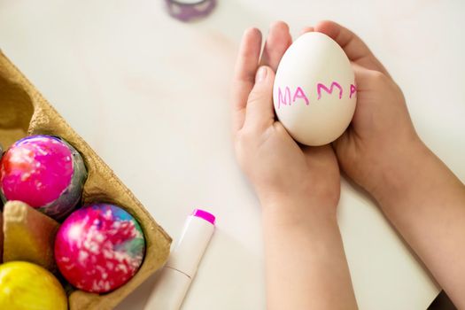 Easter egg with the inscription mom in the hands of a little girl. The process of painting eggs for Easter