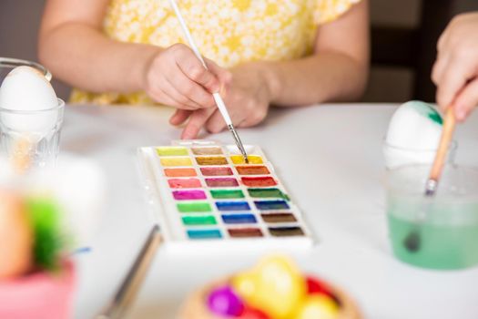 Close-up partial view of little child painting easter egg at table.