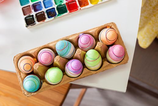 Easter eggs in a cardboard box painted for the Easter holiday on the table next to the paints