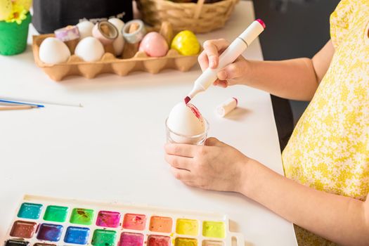 Close-up partial view of little child painting easter egg at table.