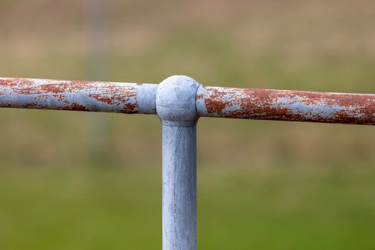 A rusty steel galvanised fence post and hand rail on a green grass background