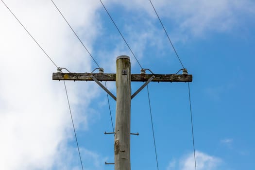 A wooden telephone pole with wires and terminal connectors in front of a bright blue sky background